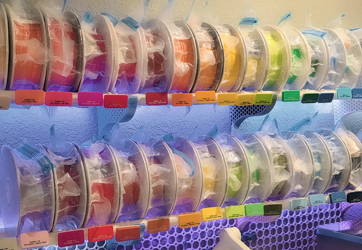 A wall of 3D printing filament spools, sorted by color